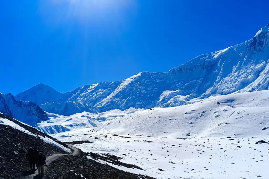 Trekkers on the Annapurna Circuit trek walking a narrow trail across a steep mountain slope in Nepal
