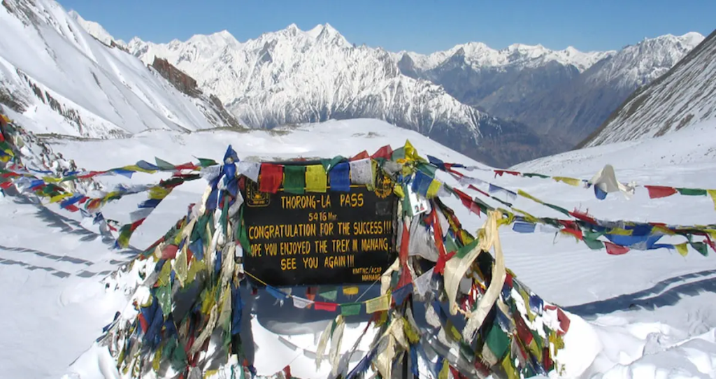 Thorong La Pass sign on the Annapurna Circuit trek in Nepal with prayer flags and snowy mountains