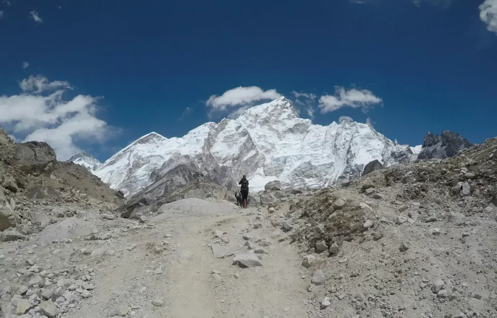 Trekkers walking along a rocky trail toward snow-covered peaks on the Everest Base Camp route