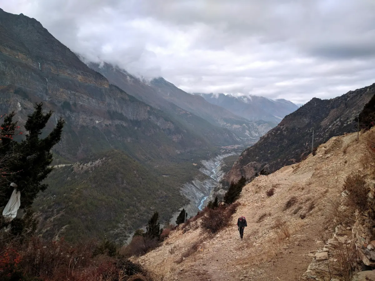 Trekking in Nepal experience on a high mountain trail with a trekker climbing above a Himalayan valley