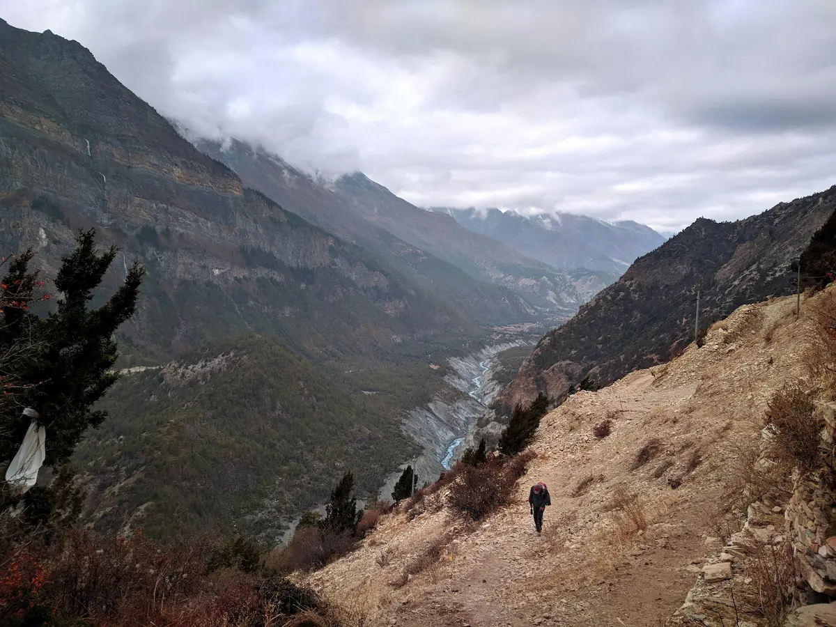 Trekking in Nepal experience on a high mountain trail with a trekker climbing above a Himalayan valley